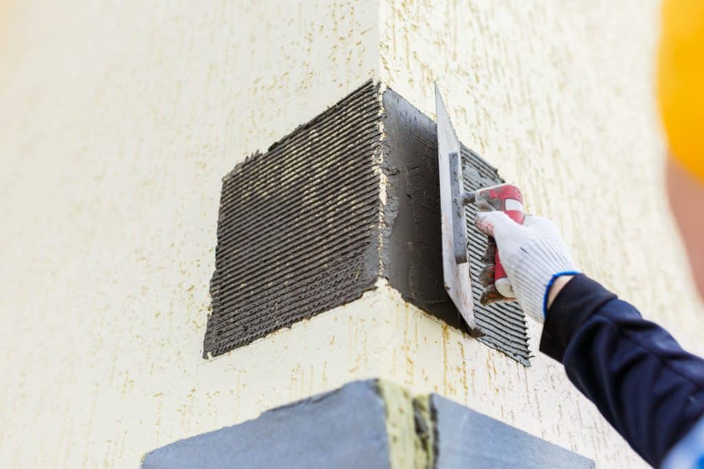 Male builder smear gray wet plaster with a spatula on the facade of the house facade